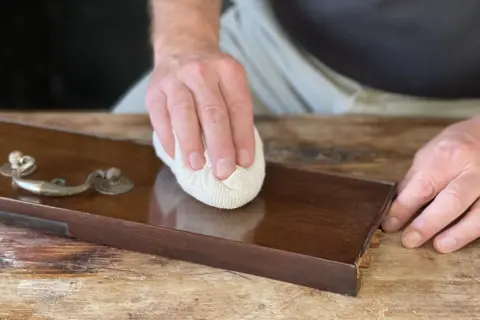 Mano lucida un mobile in legno con cera d'api, rivelando la sua bellezza naturale.