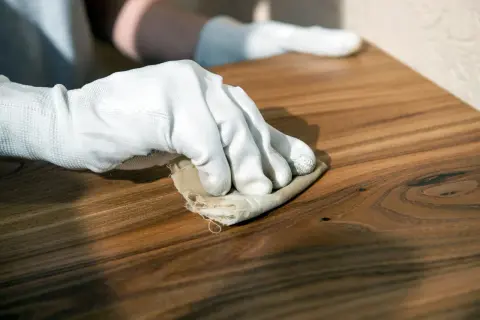 Mano guantata lucida un mobile in legno con un panno, mostrando come usare la cera d'api per una finitura naturale e protettiva.