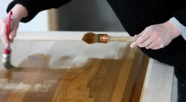 Mani che applicano vernice su un mobile in legno, mostrando come ristrutturare un mobile con cura e precisione.