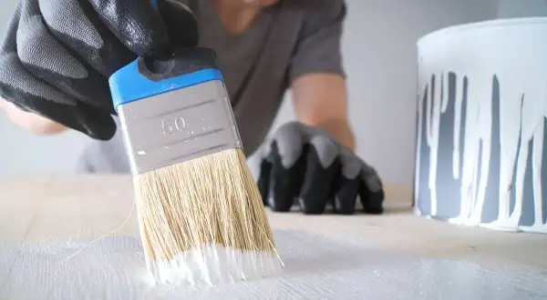 Mano guantata stende cementite bianca su una superficie di legno con un pennello.