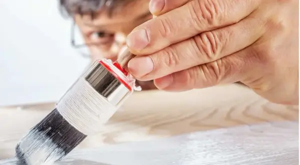 Un uomo applica il primer per legno con un pennello, preparando la superficie per la verniciatura.