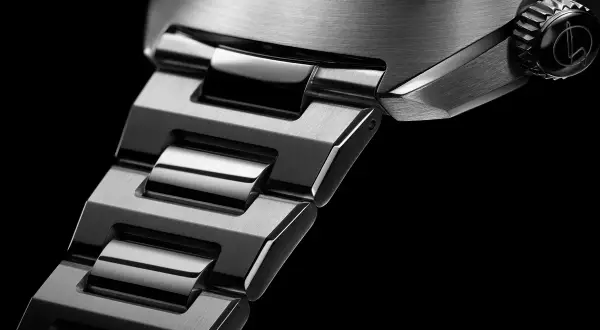 Dettaglio di un orologio con bracciale in metallo spazzolato e lucido. La corona nera presenta un logo inciso, un omaggio a un **singer reimagined**.