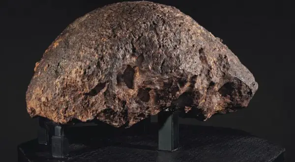 Massiccio meteorite, un esemplare di meteoriti rari, con una superficie ruvida e craterizzata, esposto su un piedistallo nero.