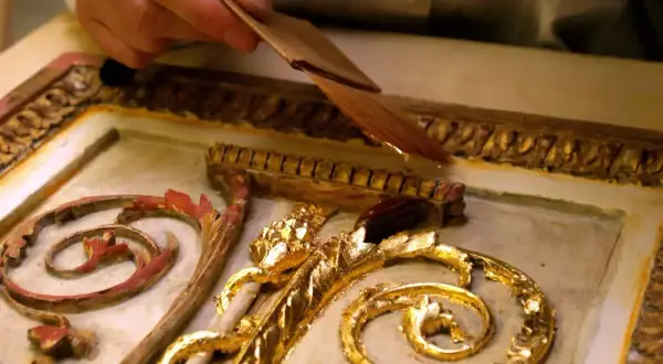 Mano applica una sottile foglia d'oro, una lega che imita l'oro, su un ornamento dorato e intagliato.