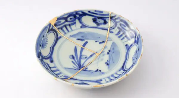 Piatto blu e bianco con crepe dorate, un esempio di tecnica del kintsugi che celebra la bellezza delle imperfezioni.