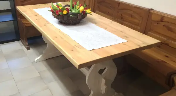 Tavolo in legno chiaro, pronto per essere lucidato, con un cestino di tulipani e una panca in legno scuro.