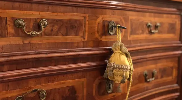 Dettaglio di mobili fine '800 con intarsi in noce e maniglie in bronzo. Un sacchetto decorativo pende da una serratura, testimoniando il loro valore storico.