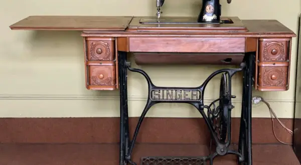Macchina da cucire Singer d'epoca, con piano in legno e cassetti intagliati. Il suo valore storico la rende un pezzo da collezione.