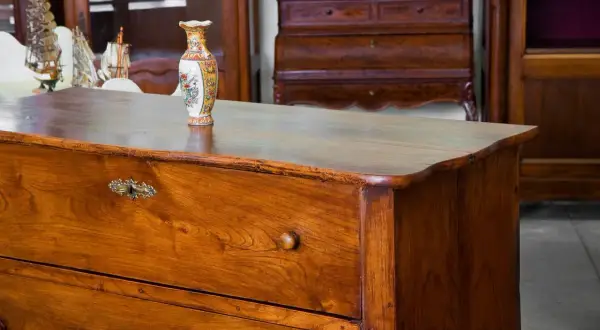 Cassettiera in legno con maniglie antiche e vaso decorato. Un esempio di come antichizzare un mobile per un tocco vintage.
