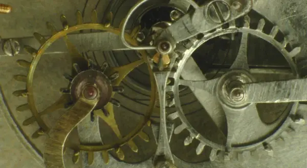 Ingranaggi dorati e argentati di un orologio, con un dettaglio dello scappamento coassiale che ne regola il movimento preciso.