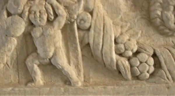 Dettaglio di un bassorilievo antico, forse parte di un restauro marmo, raffigurante figure mitologiche con drappeggi e grappoli d'uva.