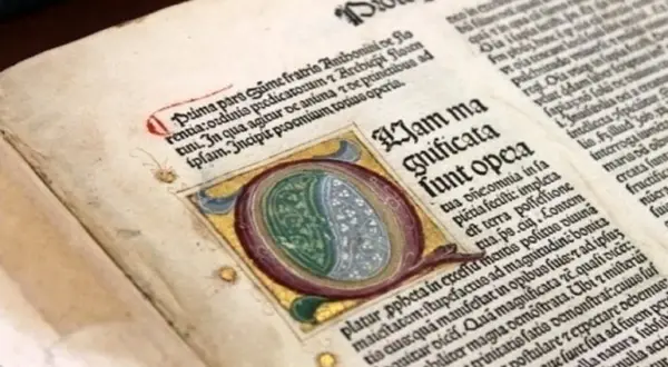 Dettaglio di antichi **primi libri stampati** con iniziale miniata e testo in latino.