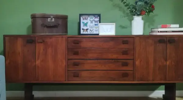 Mobile in legno scuro con cassetti e ante, decorato con una valigia vintage, quadri di farfalle e un vaso di fiori. Un esempio di restyling mobili che unisce passato e presente.