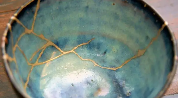 Ciotola blu con crepe dorate, un esempio di tecnica kintsugi che celebra le imperfezioni.