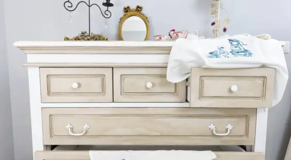 Comò in stile Chippendale rinnovato con finitura anticata. Cassetti con maniglie decorative e un ricamo di cigni su un cassetto aperto.