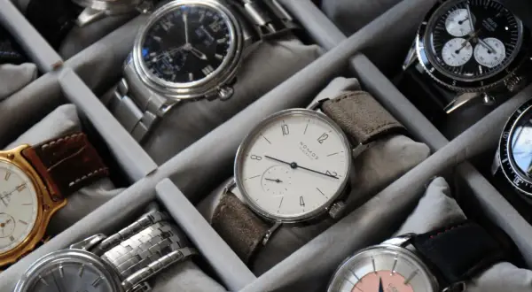Collezione di orologi in un organizer. Un orologio al quarzo come funziona, con quadrante bianco e cinturino in pelle scamosciata, è in primo piano.