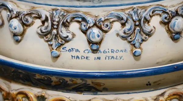 Dettaglio di un'opera in porcellana bianca e blu, con decorazioni barocche e la firma "Sofia Caltagirone Made in Italy".
