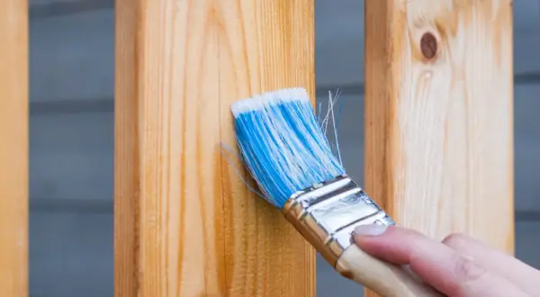 Pennello blu applica finitura a cera dopo impregnante su assi di legno.