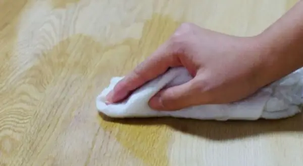 Mano che pulisce un tavolo di legno con un panno bianco, forse per sverniciare con soda caustica.