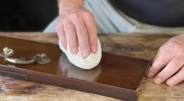 Mano lucida un mobile in legno con cera d'api, rivelando la sua bellezza naturale.