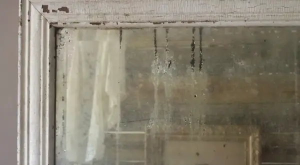 Dettagli di un vecchio specchio con cornice bianca scrostata, che riflette un ritratto e un drappo. Un esempio di come invecchiare uno specchio per un effetto anticato.
