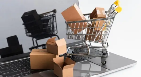 Carrello della spesa pieno di pacchi su un laptop. Il riflesso mostra un altro carrello, suggerendo un'asta online con un prezzo di riserva.
