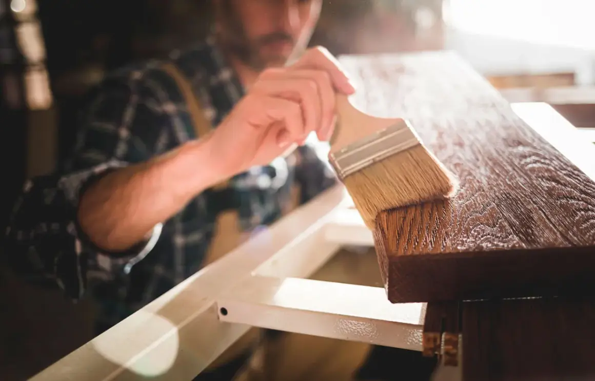 Un falegname applica una finitura su un pezzo di legno, esaltando le sue belle fibre del legno.