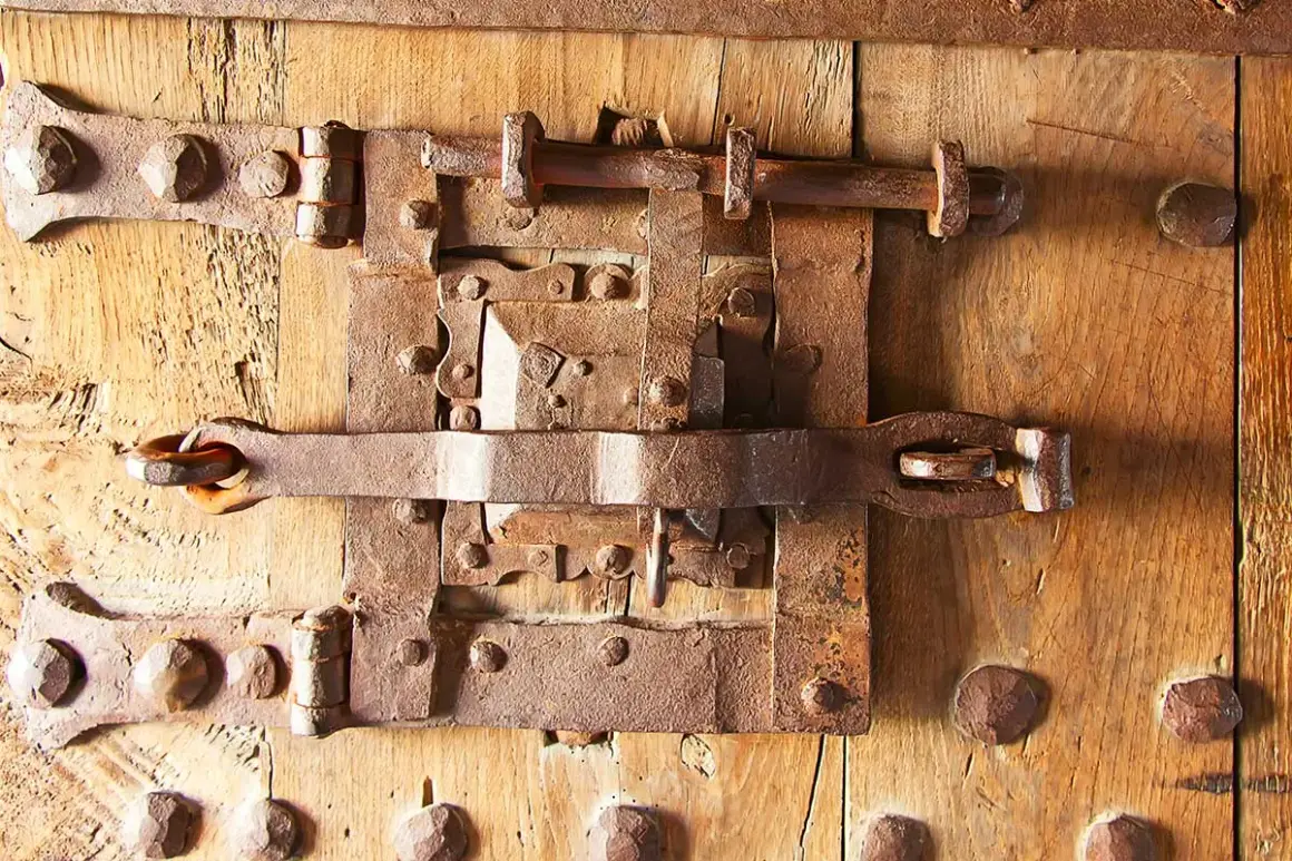 Parti di una serratura antica in ferro battuto su una porta di legno. I meccanismi arrugginiti suggeriscono una lunga storia.