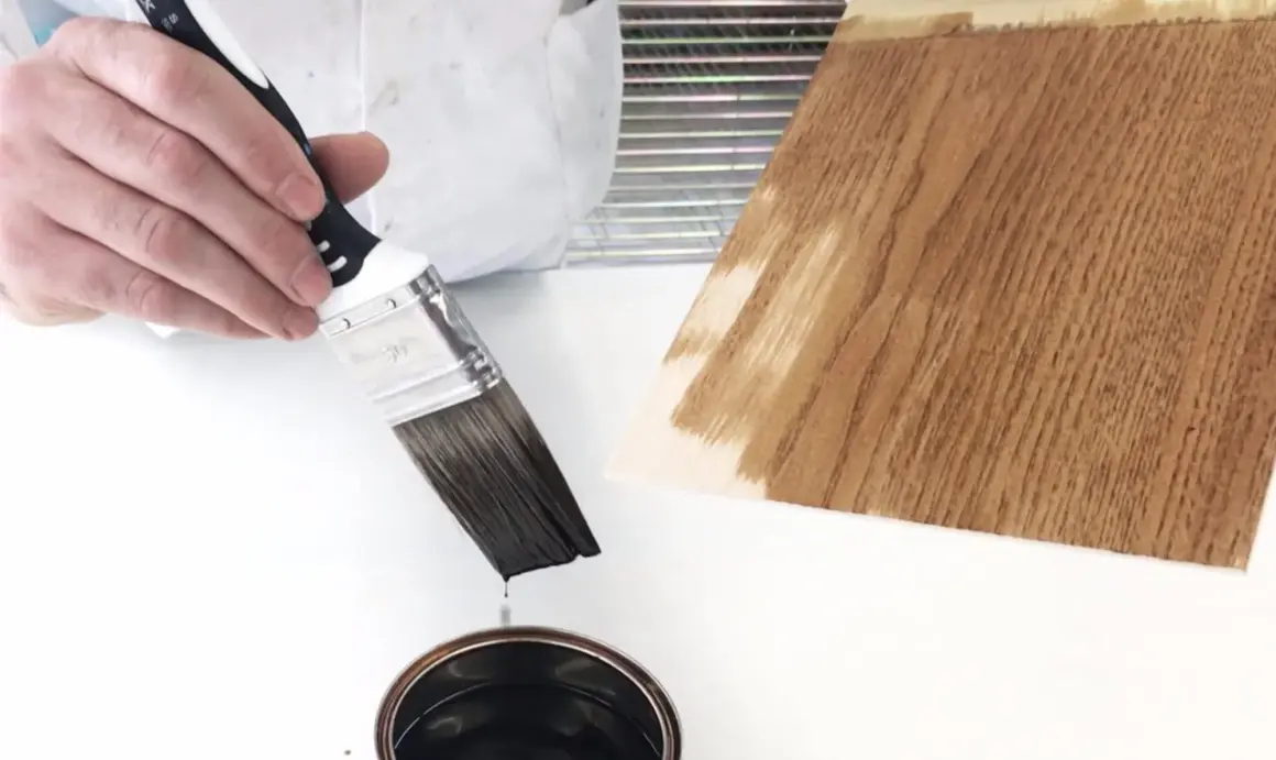 Pennello intinto in latta di impregnante, pronto per applicarlo su un campione di legno.