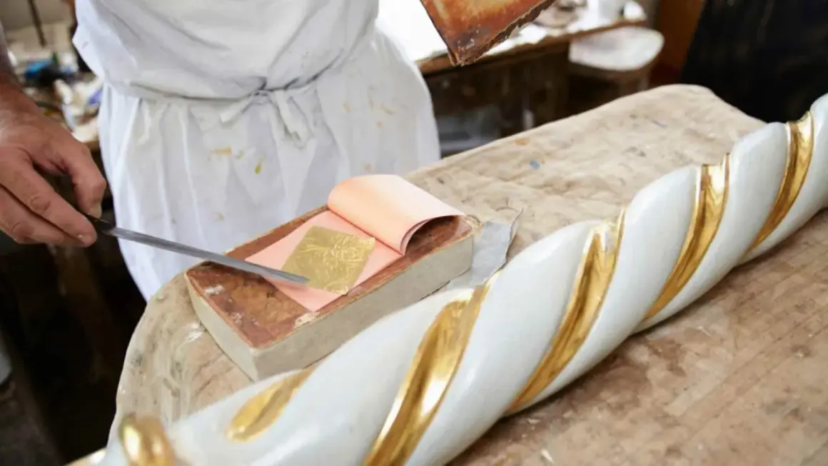 Artigiano applica foglia oro su un elemento decorativo bianco e oro. Scopri come si applica la foglia oro.
