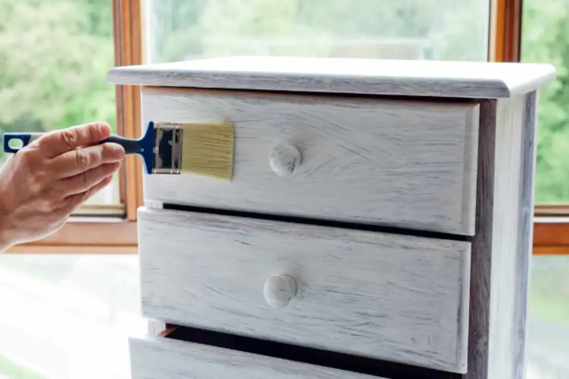Restauro di un comò con chalk paint: un pennello applica la vernice per un look shabby chic.