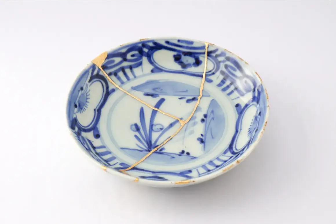 Piatto blu e bianco con crepe dorate, un esempio di tecnica del kintsugi che celebra la bellezza delle imperfezioni.