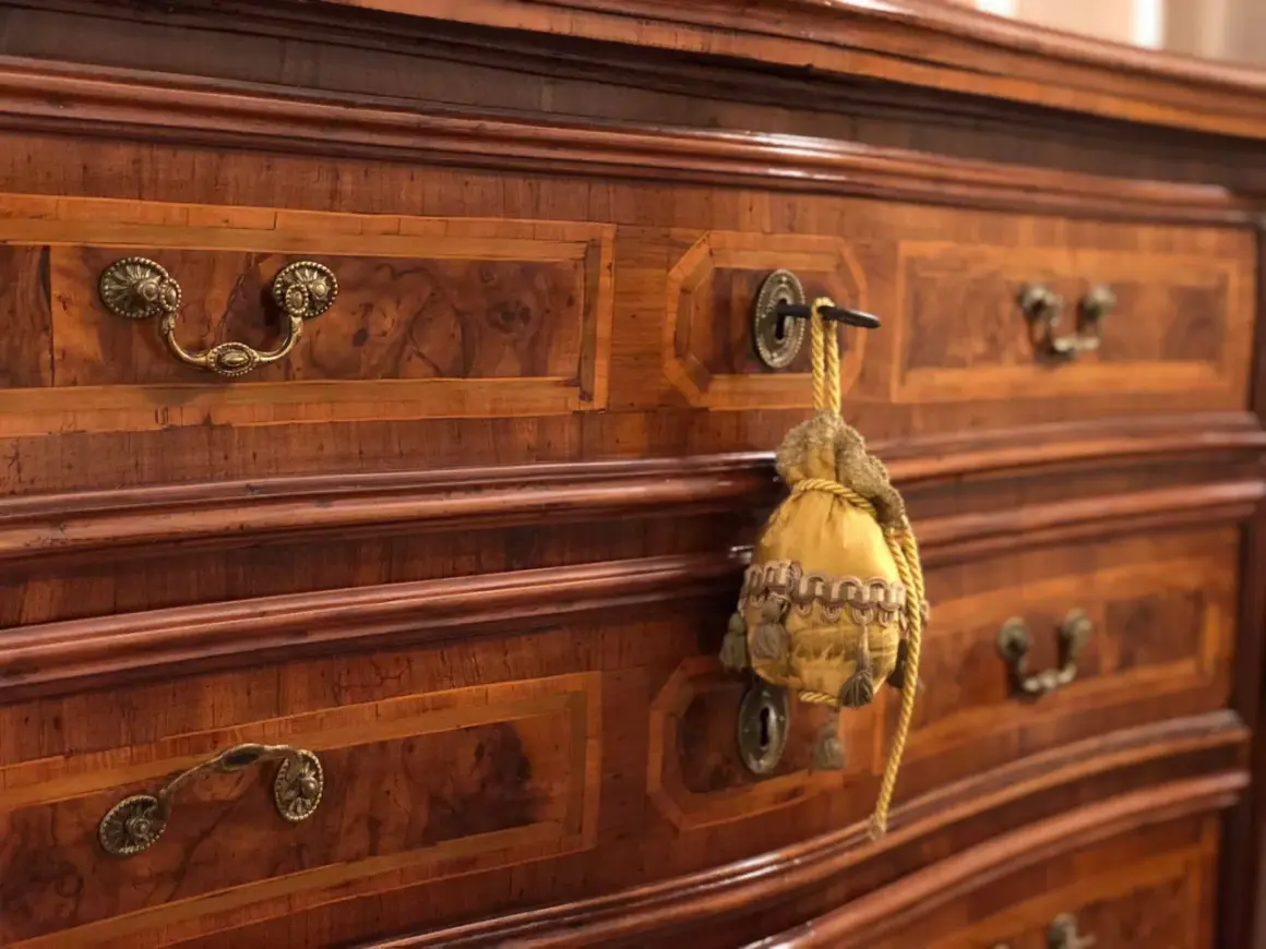 Dettaglio di mobili fine '800 con intarsi in noce e maniglie in bronzo. Un sacchetto decorativo pende da una serratura, testimoniando il loro valore storico.