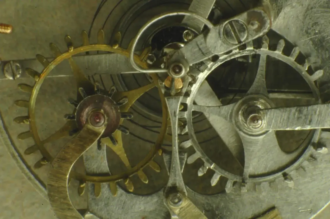 Ingranaggi dorati e argentati di un orologio, con un dettaglio dello scappamento coassiale che ne regola il movimento preciso.