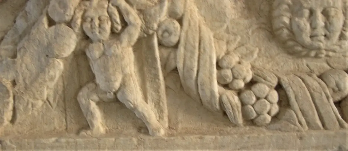 Dettaglio di un bassorilievo antico, forse parte di un restauro marmo, raffigurante figure mitologiche con drappeggi e grappoli d'uva.