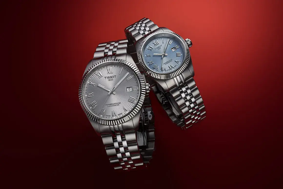 Due orologi Tissot con quadrante argentato e blu, entrambi con movimento automatico Powermatic 80, su sfondo rosso.