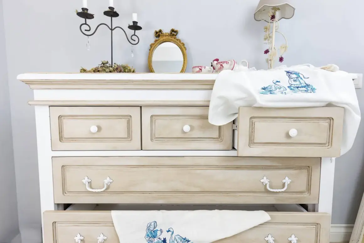 Comò in stile Chippendale rinnovato con finitura anticata. Cassetti con maniglie decorative e un ricamo di cigni su un cassetto aperto.