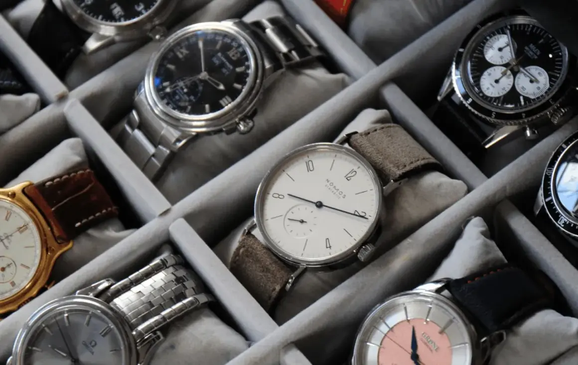 Collezione di orologi in un organizer. Un orologio al quarzo come funziona, con quadrante bianco e cinturino in pelle scamosciata, è in primo piano.