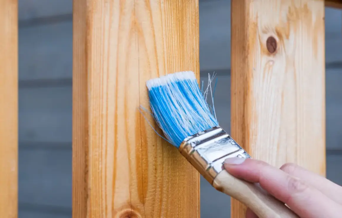 Pennello blu applica finitura a cera dopo impregnante su assi di legno.