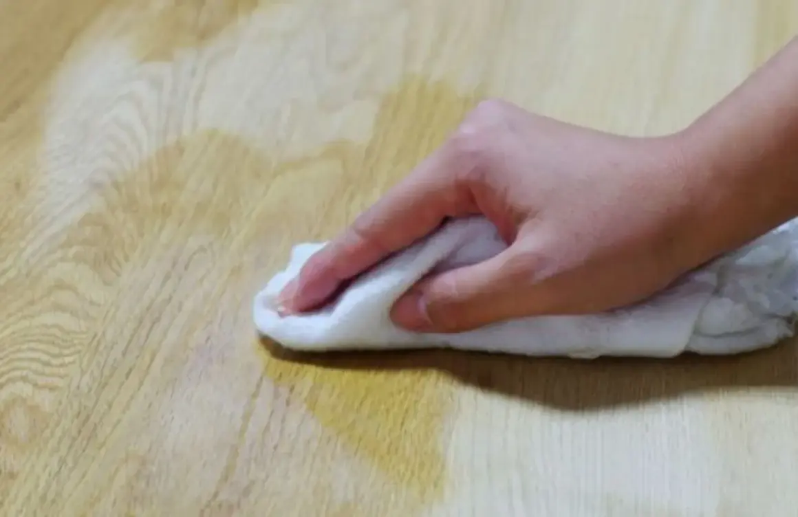 Mano che pulisce un tavolo di legno con un panno bianco, forse per sverniciare con soda caustica.