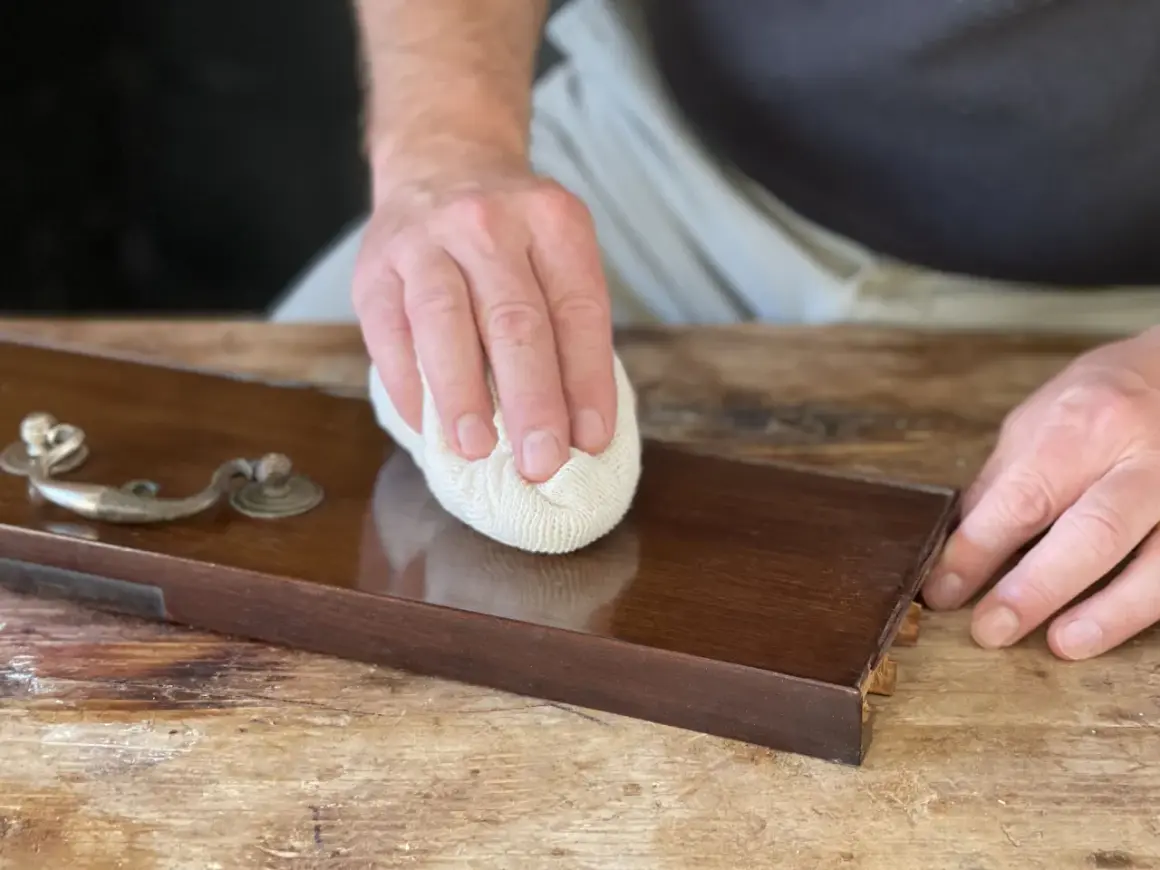 Mano lucida un mobile in legno con cera d'api, rivelando la sua bellezza naturale.