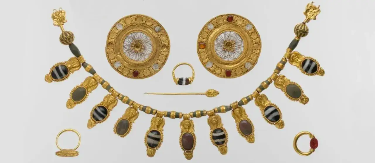 Gioielli antichi in lega che imita l'oro: collana, orecchini, anelli e spillone con pietre e decorazioni elaborate.