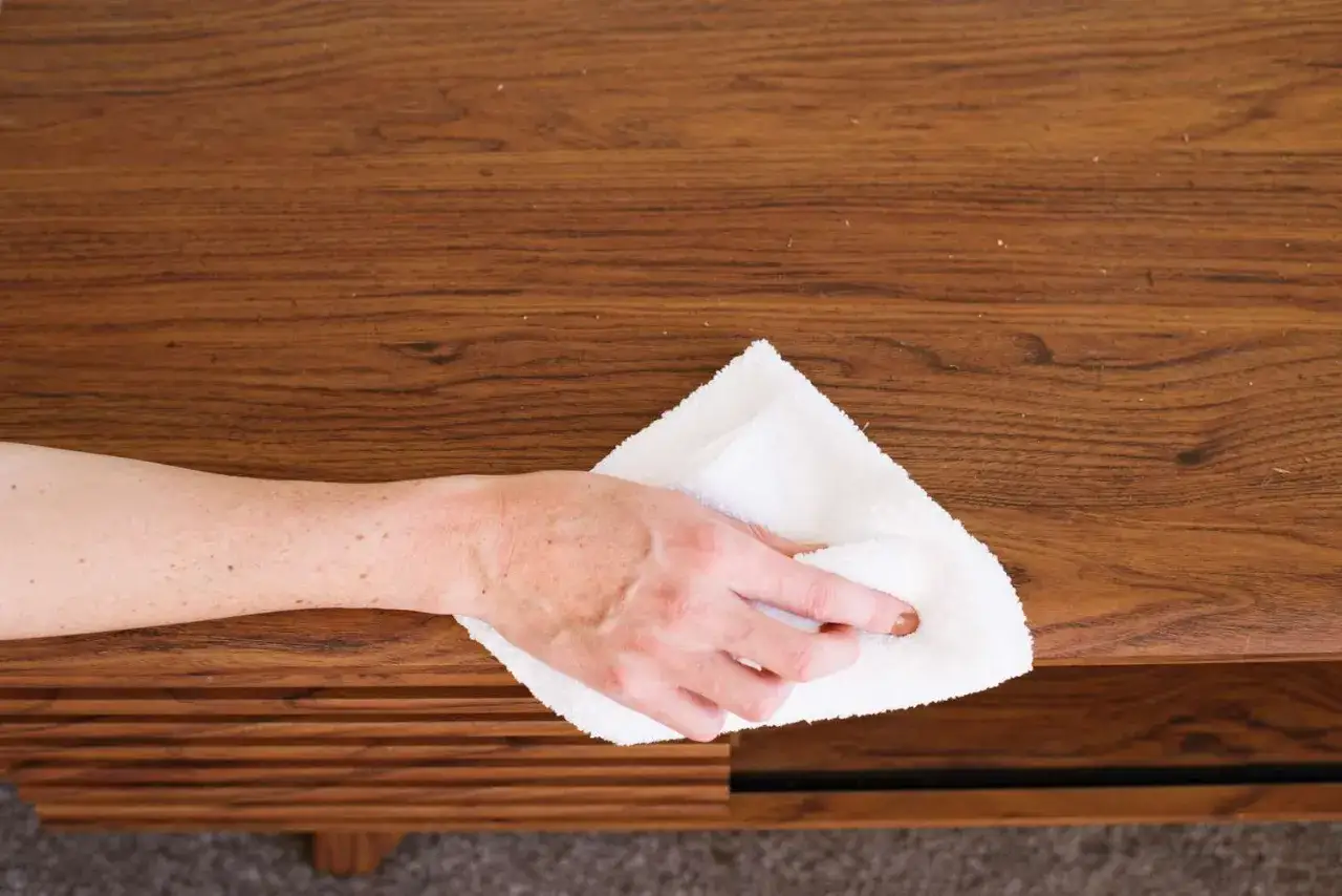 Mano che pulisce un mobile in legno con un panno bianco. Il petrolio bianco su legno dona nuova vita alla superficie.