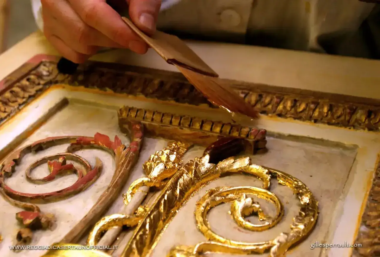 Mano esperta applica la foglia d'oro su un ornamento barocco, un dettaglio di doratura foglia oro che dona preziosit&agrave;.