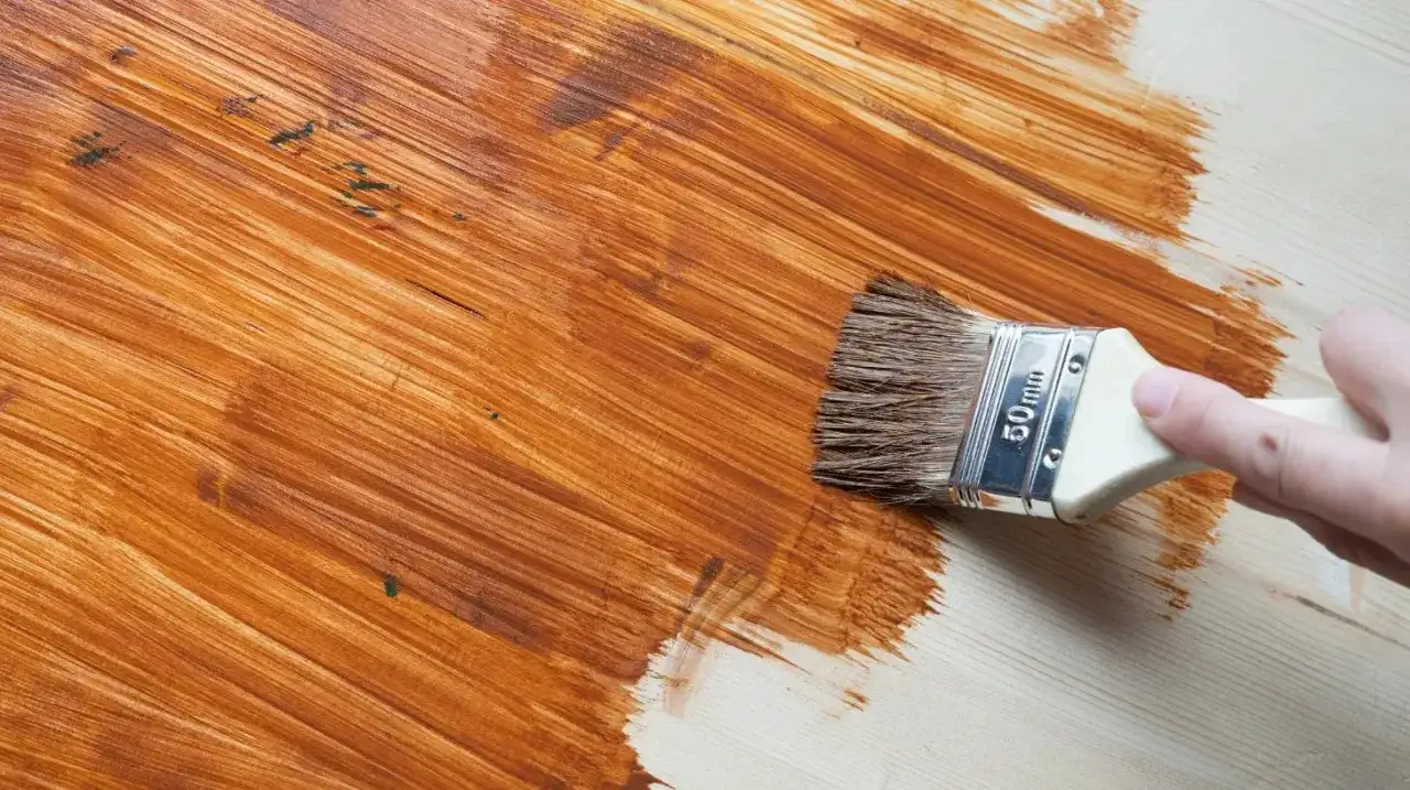Pennello applica una mano di vernice marrone su legno chiaro. Questo è cos'è il primer per legno: prepara la superficie per una finitura perfetta.