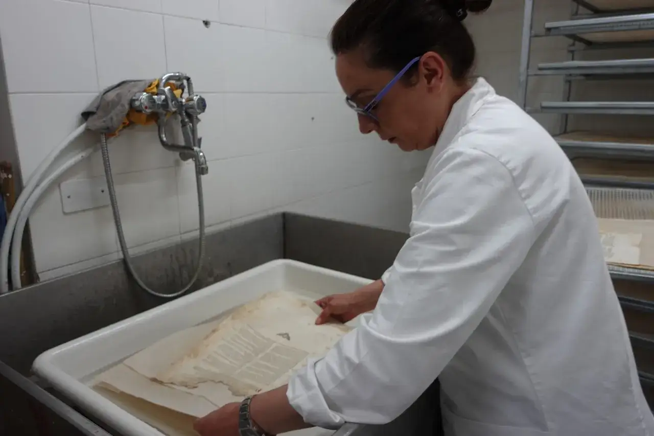 Donna con camice bianco restaura fogli ingialliti, un passo fondamentale per la rilegatura libri vecchi.