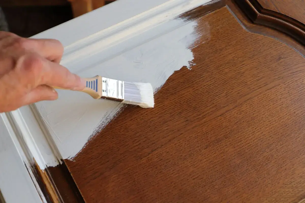 Mano che stende cementite su una porta di legno scuro, trasformandola con un tocco di bianco.