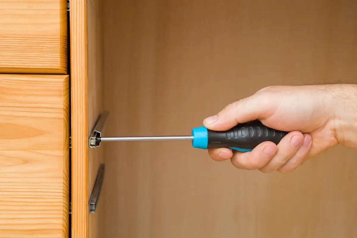 Mano con cacciavite che lavora su guide per cassetti in legno.