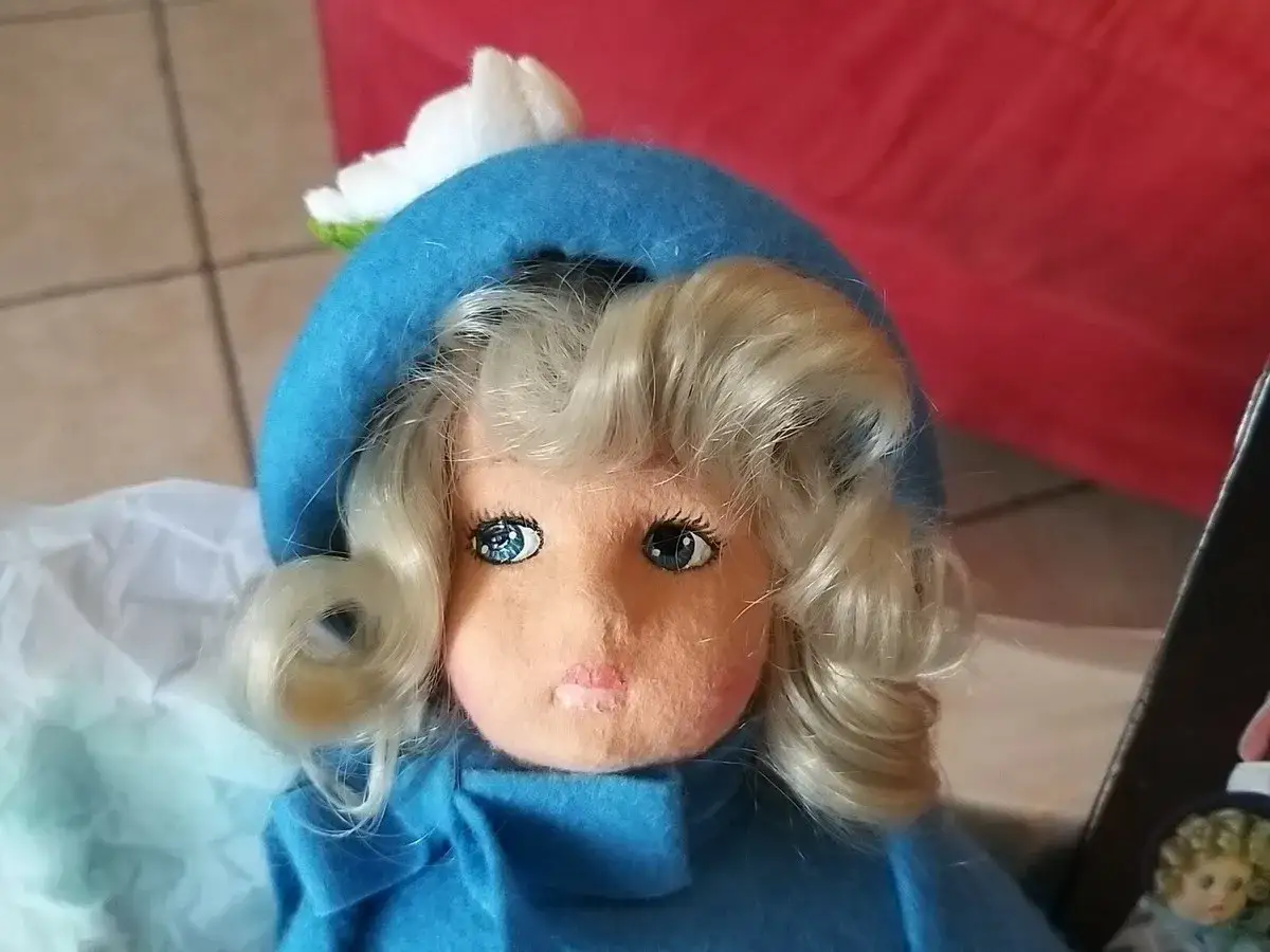 Bambole Lenci: come riconoscerle. Una bambola con cappello blu e fiore bianco, capelli biondi ricci, occhi azzurri.
