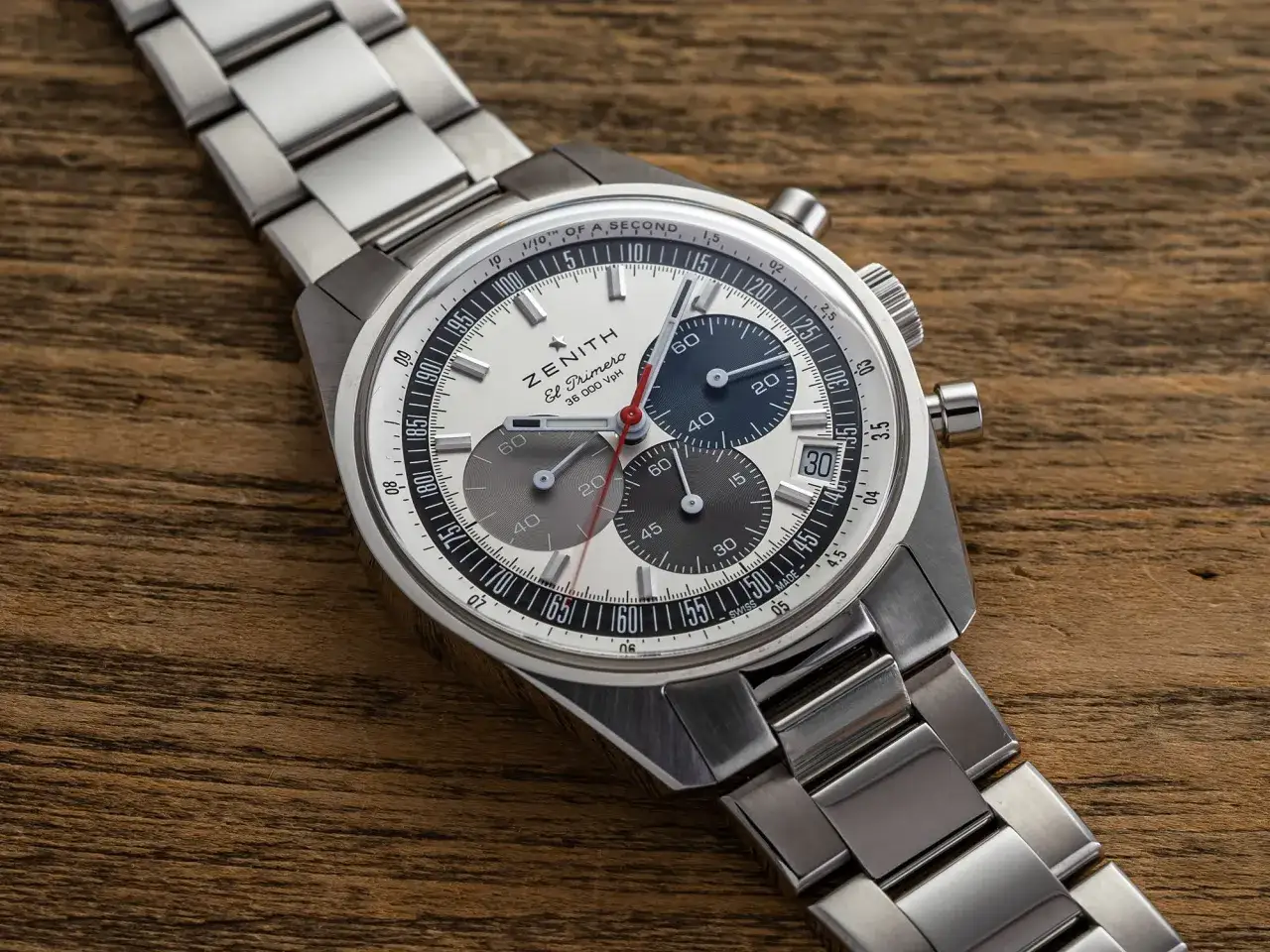 Orologio Zenith El Primero con quadrante bianco, contatori grigi e blu, e cinturino in acciaio su sfondo di legno.